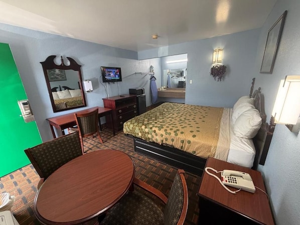 A hotel room with a bed, a desk with a telephone, a chair, a table, and a television.