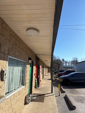 A building with a brick facade, a covered walkway, and a parking lot with cars. - TRAVEL INN (Richmond)