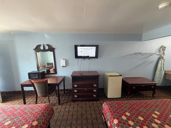 Une chambre d’hôtel avec deux lits, un bureau avec un ordinateur, un miroir, une télévision et un petit réfrigérateur.