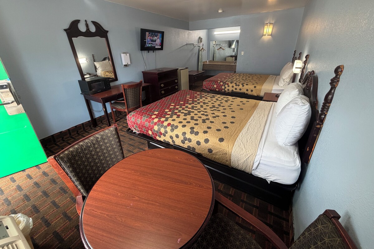 A hotel room with a bed, a desk, a chair, a round table, a television, and a mirror.