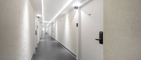 A long, narrow hotel corridor with white walls and a grey carpet.