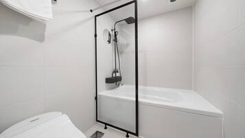 Un baño moderno con ducha de vidrio, bañera blanca y retrete.