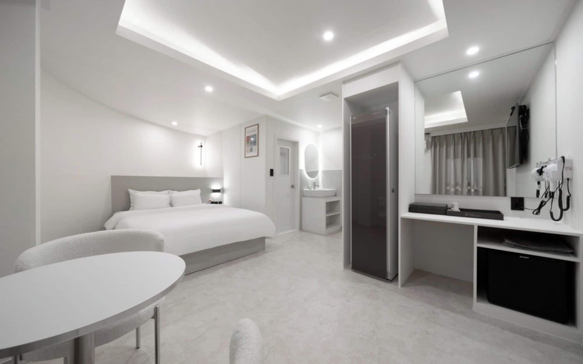 A modern hotel room with a bed, bedside table, and a desk area with a mirror.