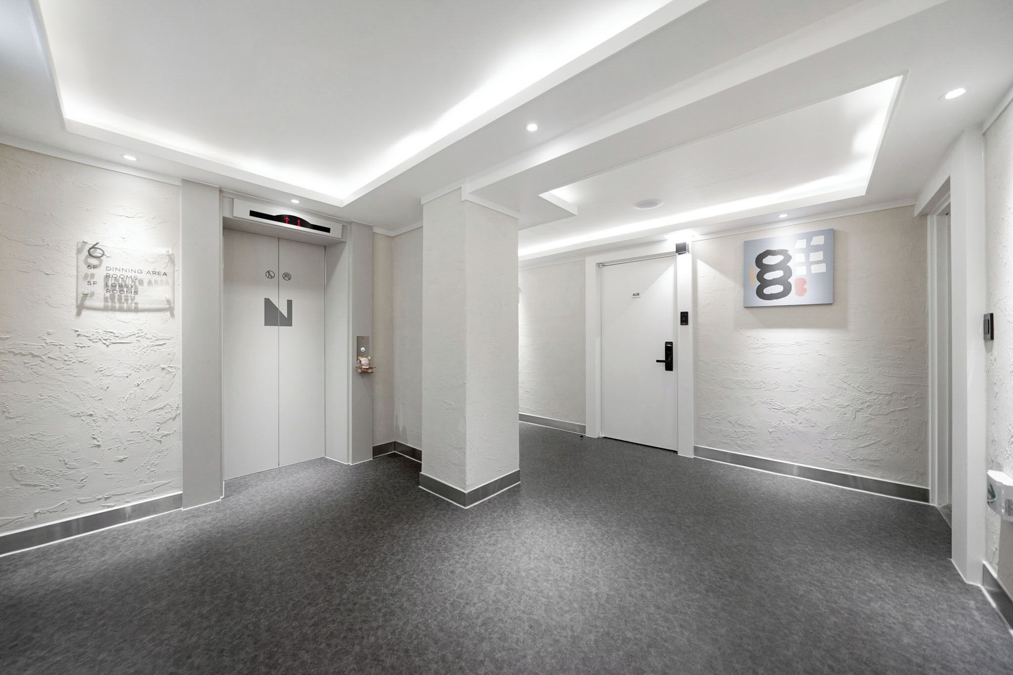 Un pasillo moderno de hotel con alfombra gris, paredes blancas e iluminación empotrada en el techo.