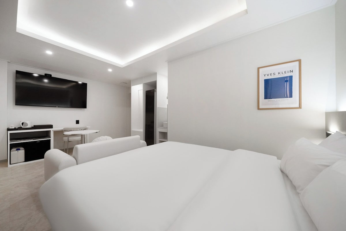 Una habitación de hotel moderna con una cama grande, un escritorio, un televisor de pantalla plana y una obra enmarcada de Yves Klein en la pared.