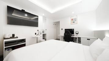 Una habitación de hotel moderna con una cama grande, un escritorio con silla, un televisor de pantalla plana, un espejo y una mesita de noche con lámpara.