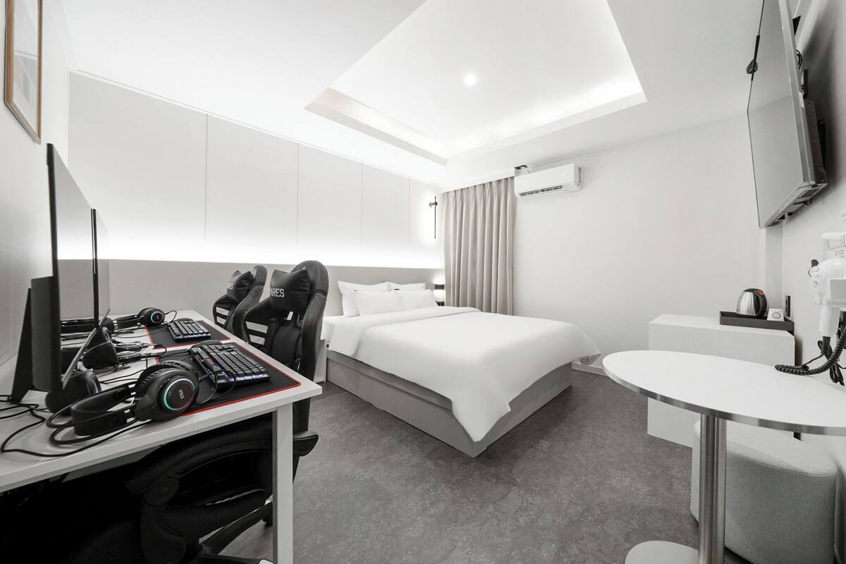 Ein modernes Hotelzimmer mit Schreibtisch, Computer, Kopfhörern und einem Bett.