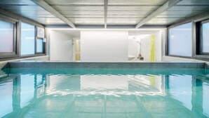 Una piscina con agua cristalina, rodeada por una solana empavedada y amplias ventanas.