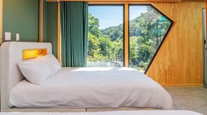 Ein modernes Schlafzimmer mit einem großen Bett, einer Kopfteilbeleuchtung und Blick auf einen Wald durch ein großes Fenster.