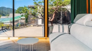 Un salon moderne avec un canapé et une petite table, de grandes fenêtres offrant une vue sur un immeuble et des arbres.