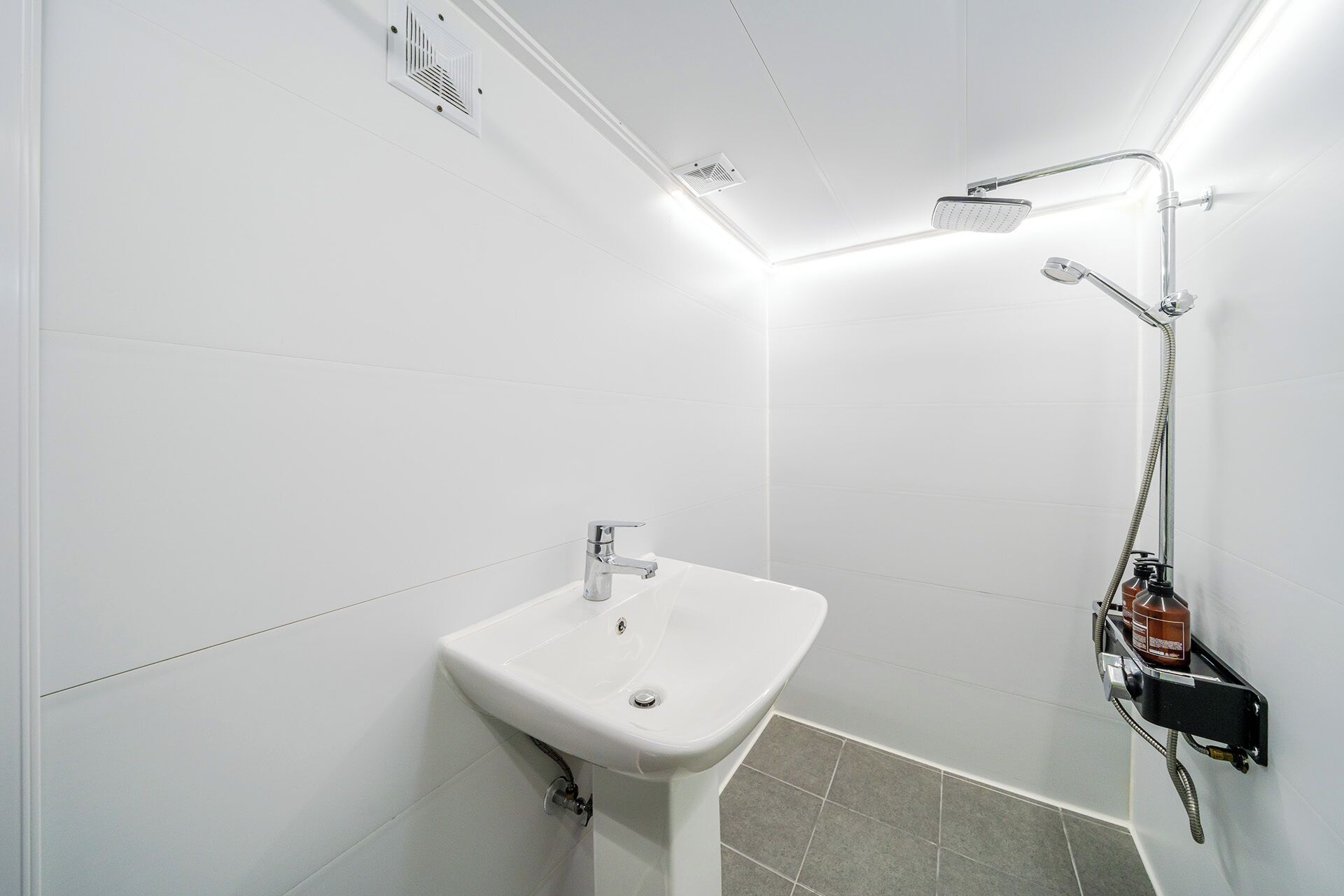 A bathroom with a white sink, a shower with a handheld showerhead, and a wall-mounted heater.