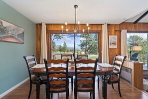 Ein Esszimmer mit Holztisch und -stühlen, einer Kronleuchter und Blick ins Freie.
