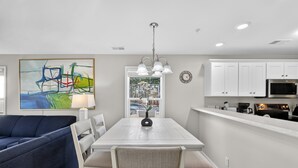 A modern kitchen with white cabinets, a dining table, and a blue sofa. - Myrtle Beach River Oaks 30F (Myrtle Beach)