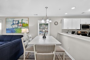 A modern kitchen with white cabinets, a dining table, and a blue sofa. - Myrtle Beach River Oaks 30F (Myrtle Beach)
