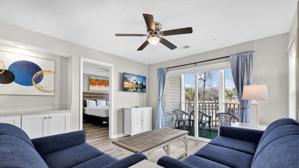 A modern living room with a ceiling fan, a dining table, and blue upholstered chairs. - Myrtle Beach River Oaks 30F (Myrtle Beach)