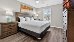 A bedroom with a bed, wooden nightstands, a ceiling fan, a window with a view, and a dresser. - Myrtle Beach River Oaks 30F (Myrtle Beach)