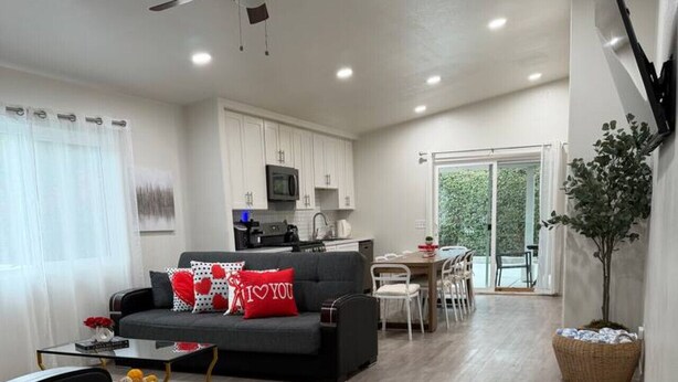 A modern living room with a sofa, coffee table, and a dining area with a table and chairs. - The Coachella Gem with Spa and Fire-pit sleeps 14 (Coachella)