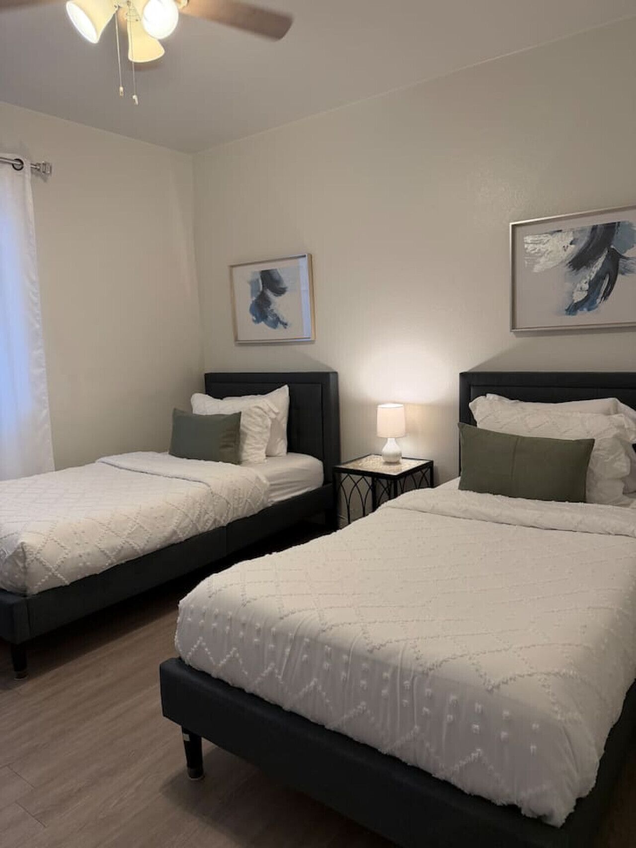 Ein Hotelzimmer mit zwei Betten, einem Deckenventilator, Kunstwerken an den Wänden und einem Nachttisch mit Lampe.