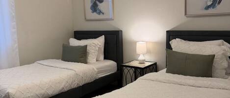 Ein Hotelzimmer mit zwei Betten, einem Deckenventilator, Kunstwerken an den Wänden und einem Nachttisch mit Lampe.