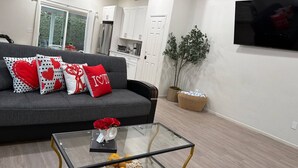 A living room with a grey sofa, a glass coffee table, and a flat-screen TV mounted on the wall. - The Coachella Gem with Spa and Fire-pit sleeps 14 (Coachella)