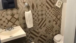 Un bagno con piastrelle decorate, un lavandino, uno specchio, un portascopevoli e un water.