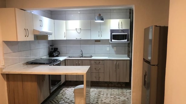 Una cucina compatta con mobili bianchi, un forno a microonde, un frigorifero e un tavolo di legno.