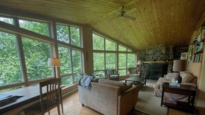 A cozy living room with a fireplace, wooden floors, and large windows offering a view of the outdoors. - Lakefront 5-Bedroom Chalet in Mont-Blanc - Monthly Rental (Laurentians) (Mont-Blanc)