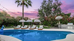 Une piscine entourée de chaises longues et de parasols, le tout baigné d’une végétation luxuriante et agrémenté de plantes en fleurs.