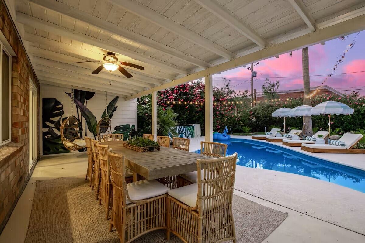 Um pátio externo com piscina, móveis de vime e luzes de fada.