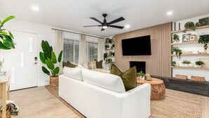 Un salon moderne avec un canapé blanc, un ventilateur de plafond, un téléviseur à écran plat fixé au mur et une cheminée.