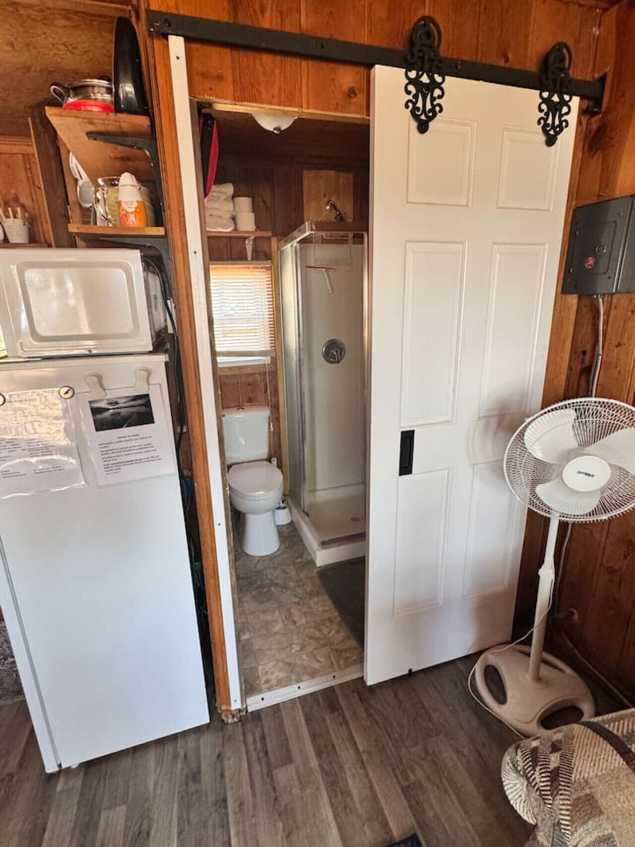 Une petite salle de bain équipée d’une douche, de toilettes et d’un réfrigérateur blanc.