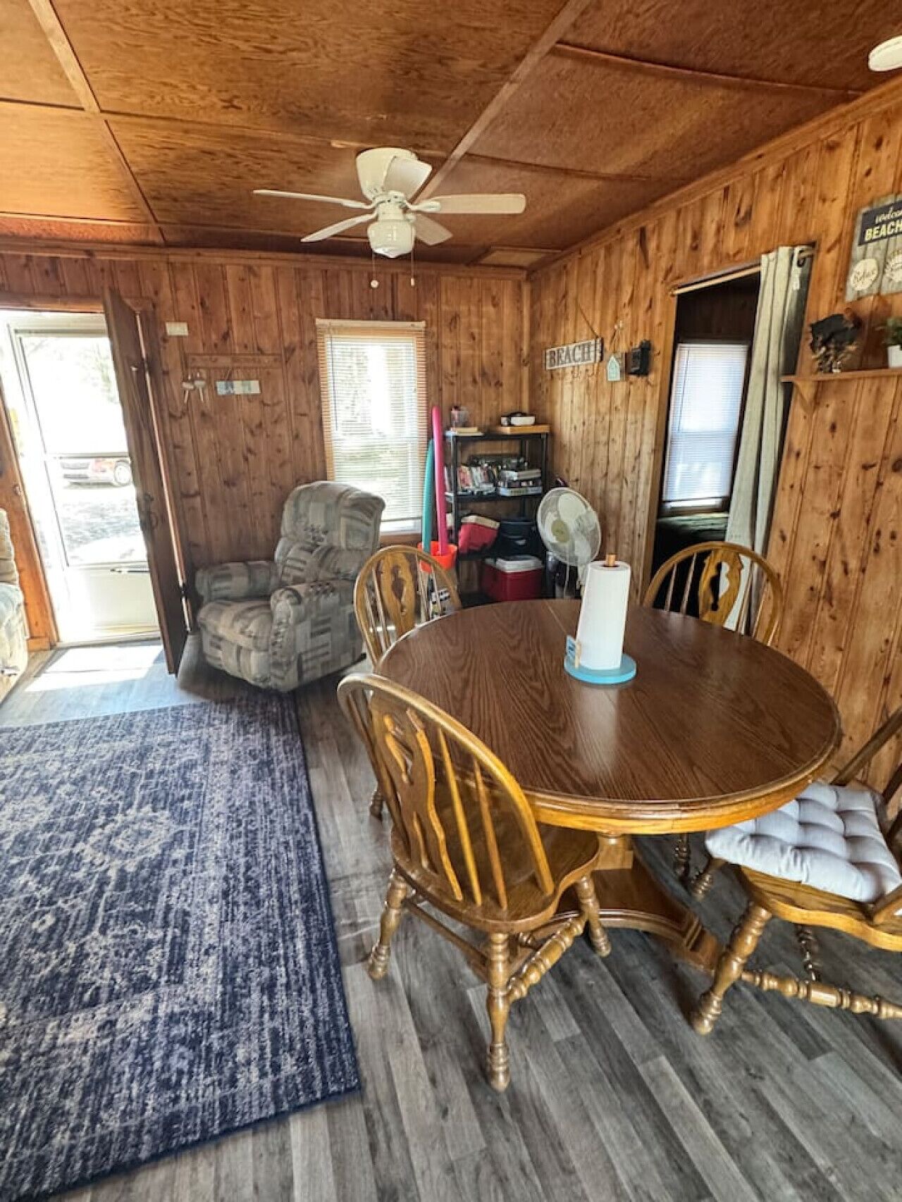 Un intérieur en bois avec une table de salle à manger ronde, quatre chaises, un ventilateur de plafond et une bibliothèque.