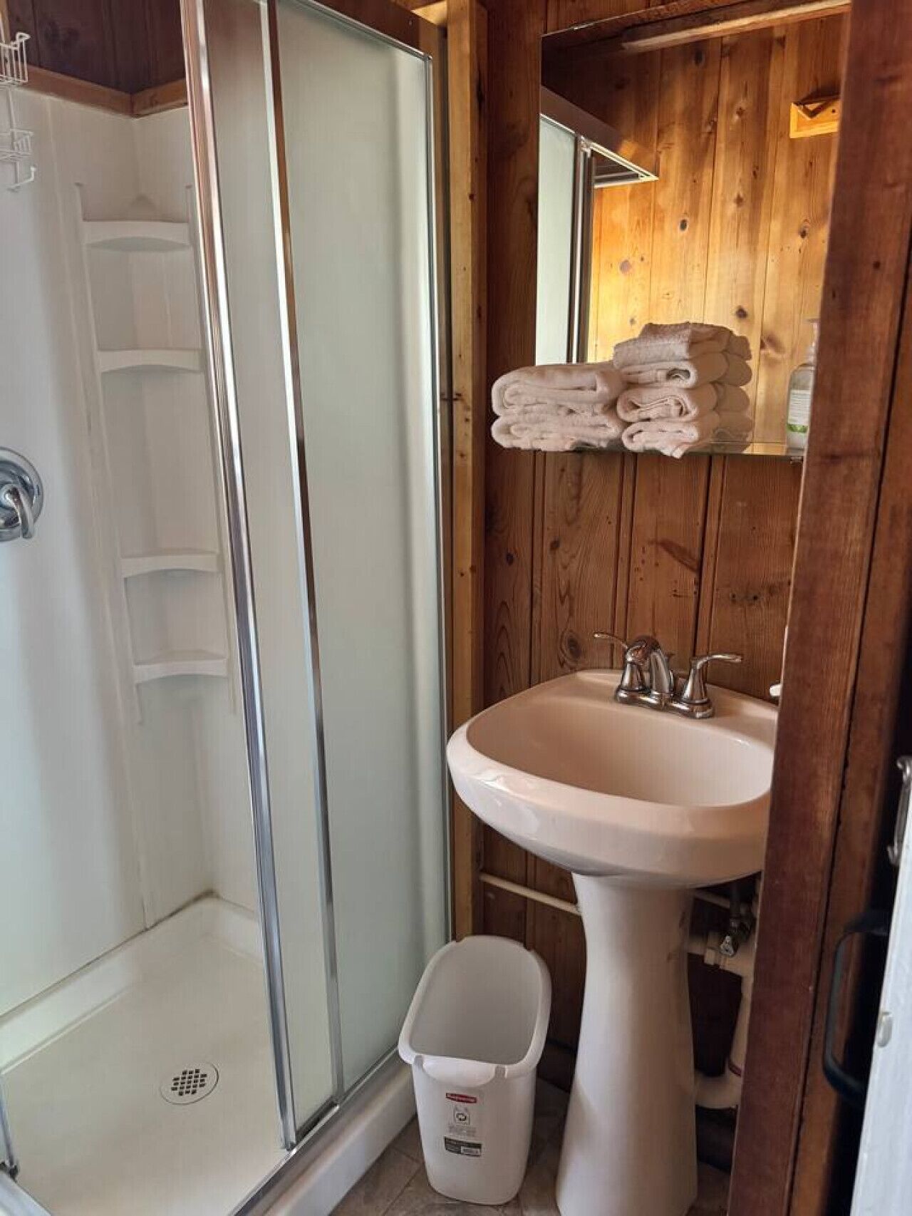 A bathroom with a glass-enclosed shower, a pedestal sink, and a wooden vanity with a mirror.