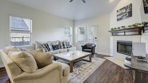 Een woonkamer met een bank, fauteuil, salontafel, open haard en plafondventilator.