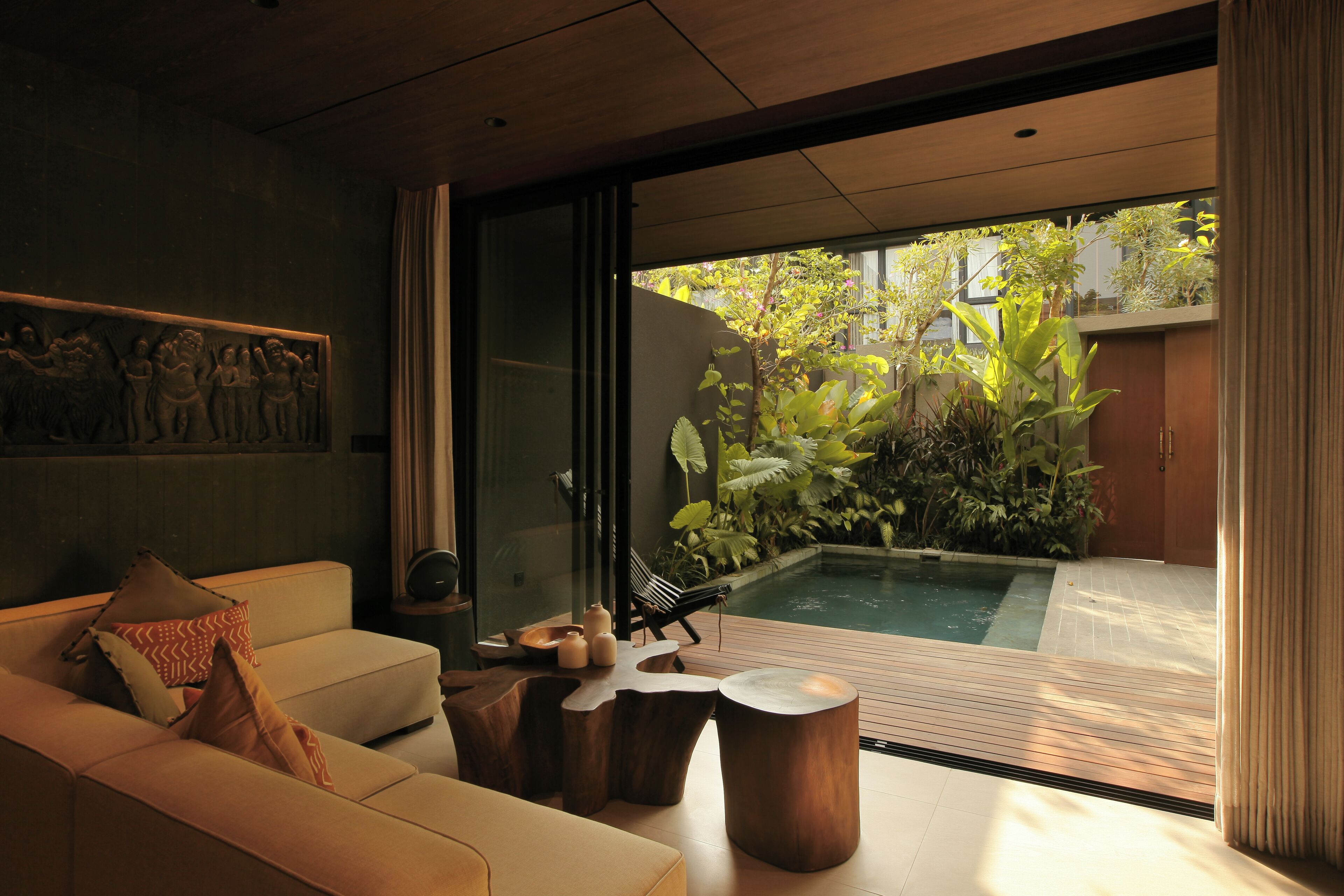 A modern interior with a sofa, wooden side tables, and a small pool area with plants.