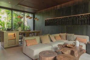 A modern living room with a sectional sofa, wooden coffee table, and a dining area with a wooden table and chairs. - The Akasha Berawa Luxury Villas (Tibubeneng)