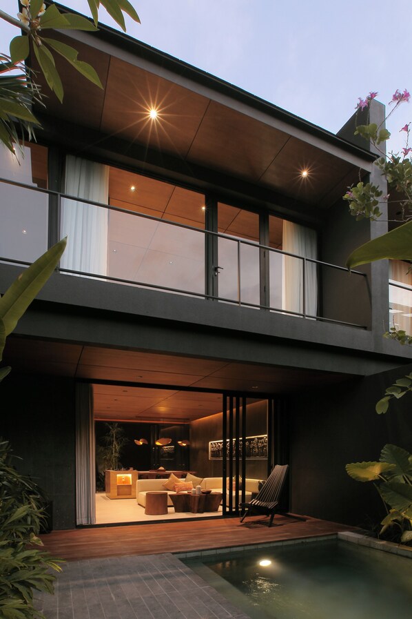 Uma casa moderna de dois andares com varanda, piscina e interior bem iluminado.
