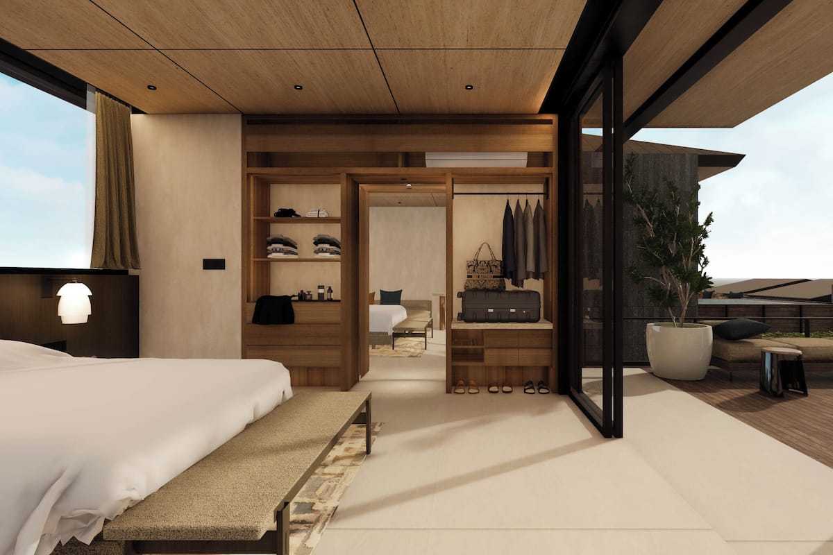 A modern hotel room with a large bed, a walk-in closet, a seating area with a view, and a balcony with a potted plant.