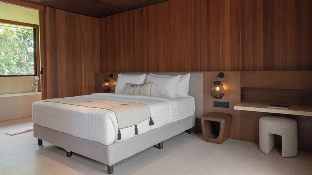 Une chambre à coucher moderne avec un grand lit, des lampes de chevet, un petit tabouret et un panneau mural en bois.