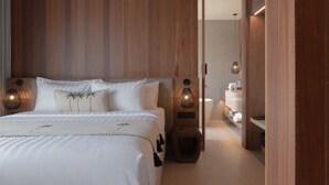 A modern hotel room with a wooden headboard, a bed with white linens, a nightstand with a lamp, and a small seating area with a stool. - The Akasha Berawa Luxury Villas (Tibubeneng)