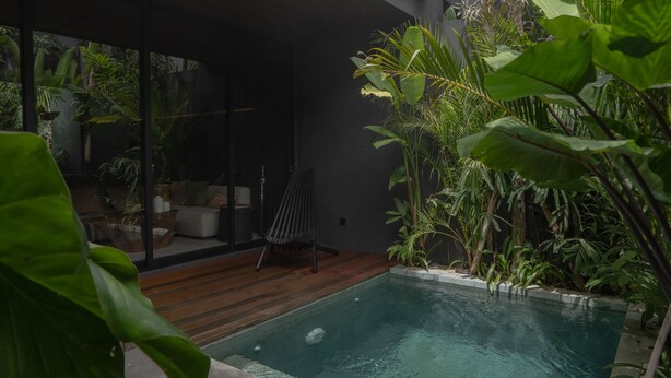 A modern outdoor pool area with a wooden deck, lounge seating, and lush tropical plants. - The Akasha Berawa Luxury Villas (Tibubeneng)
