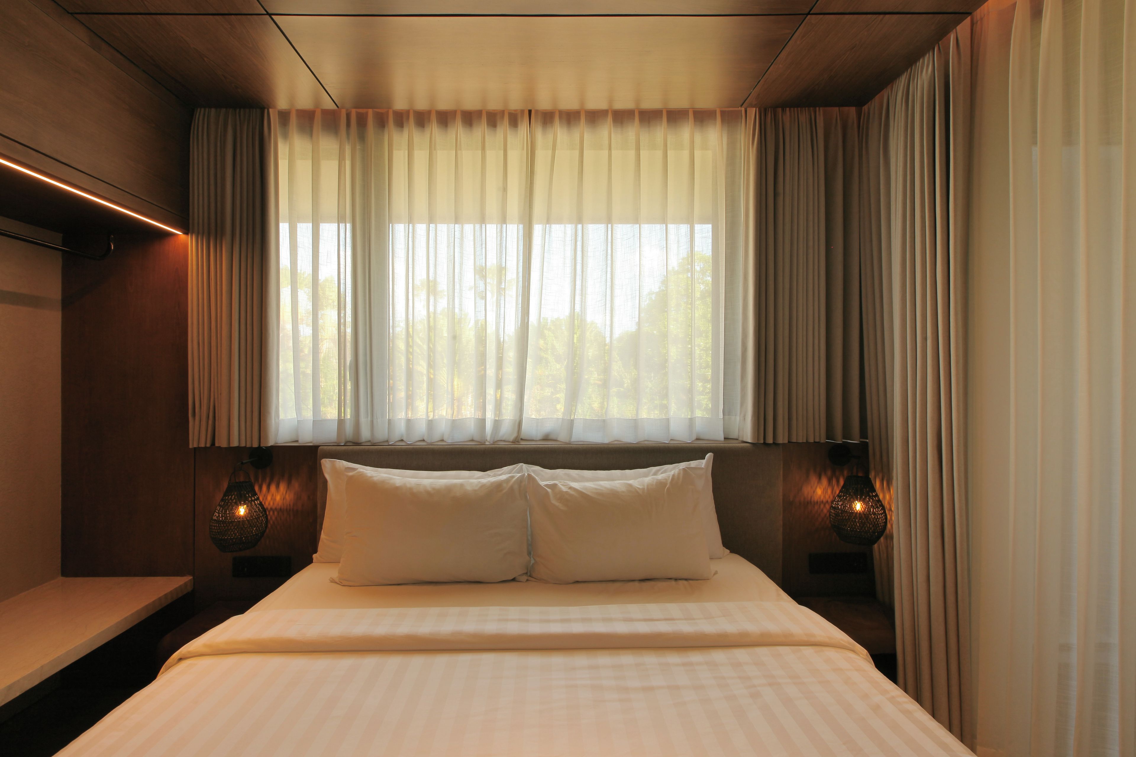 Een hotelkamer met een bed, twee bedlampen en een raam met gordijnen.