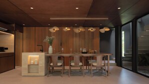 Une cuisine moderne avec des meubles en bois, un îlot central doté de sièges, un éclairage suspendu et une vue dégagée grâce à de grandes fenêtres.