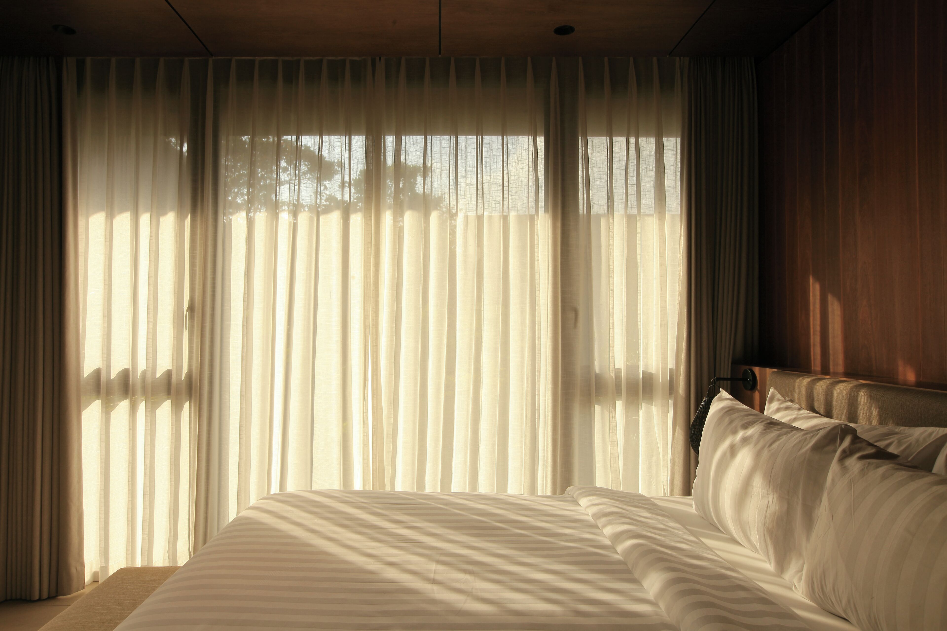 Habitación de hotel con una cama grande, cortinas traslúcidas y vistas al exterior.
