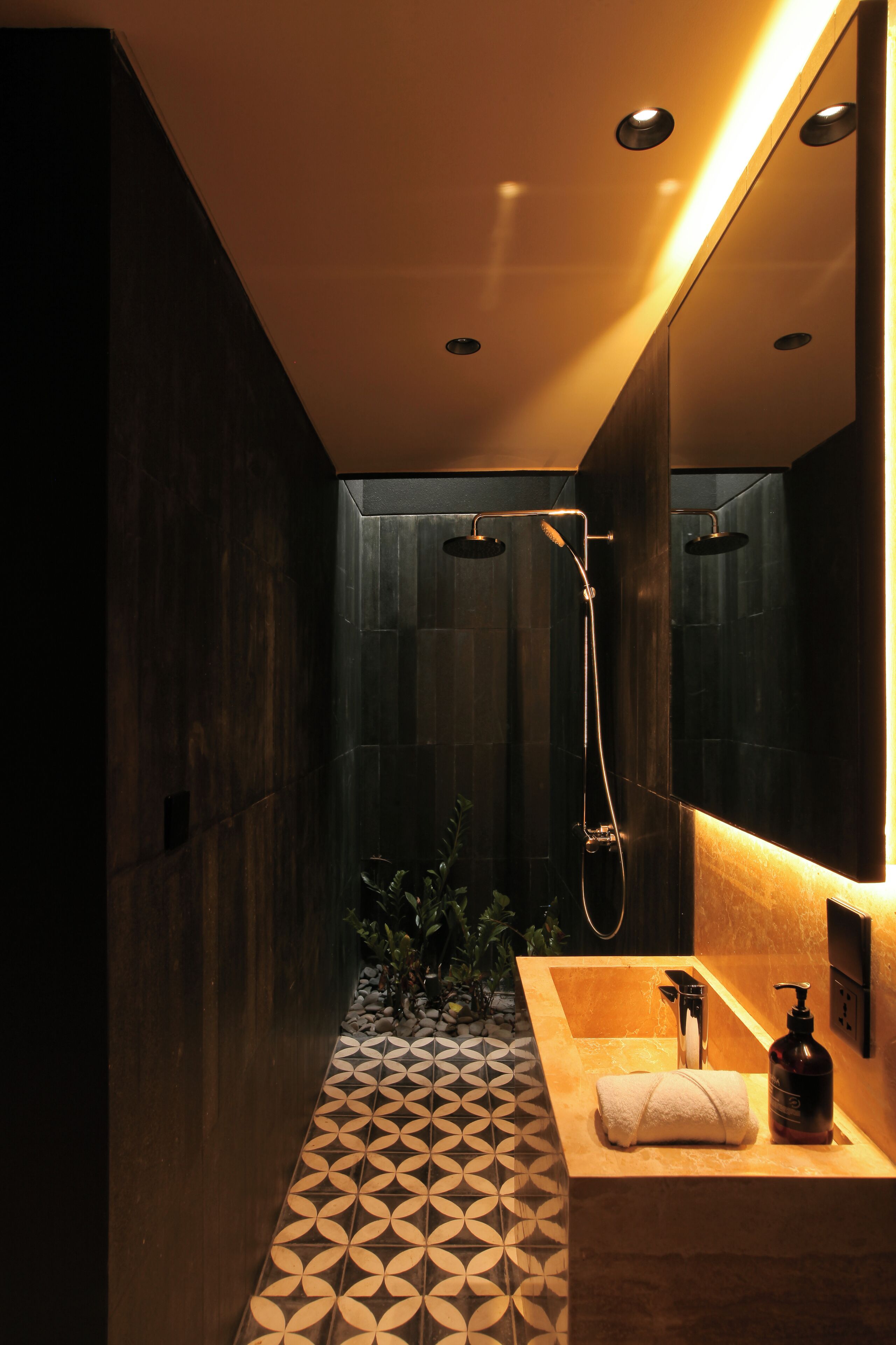 A modern bathroom with a geometric patterned floor, a wooden vanity with a towel, a handheld showerhead, and a large mirror.