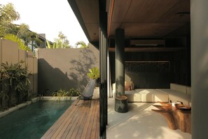 Uma área moderna de piscina ao ar livre com deck de madeira, espreguiçadeira e espaço de estar com sofá e mesinha de centro.