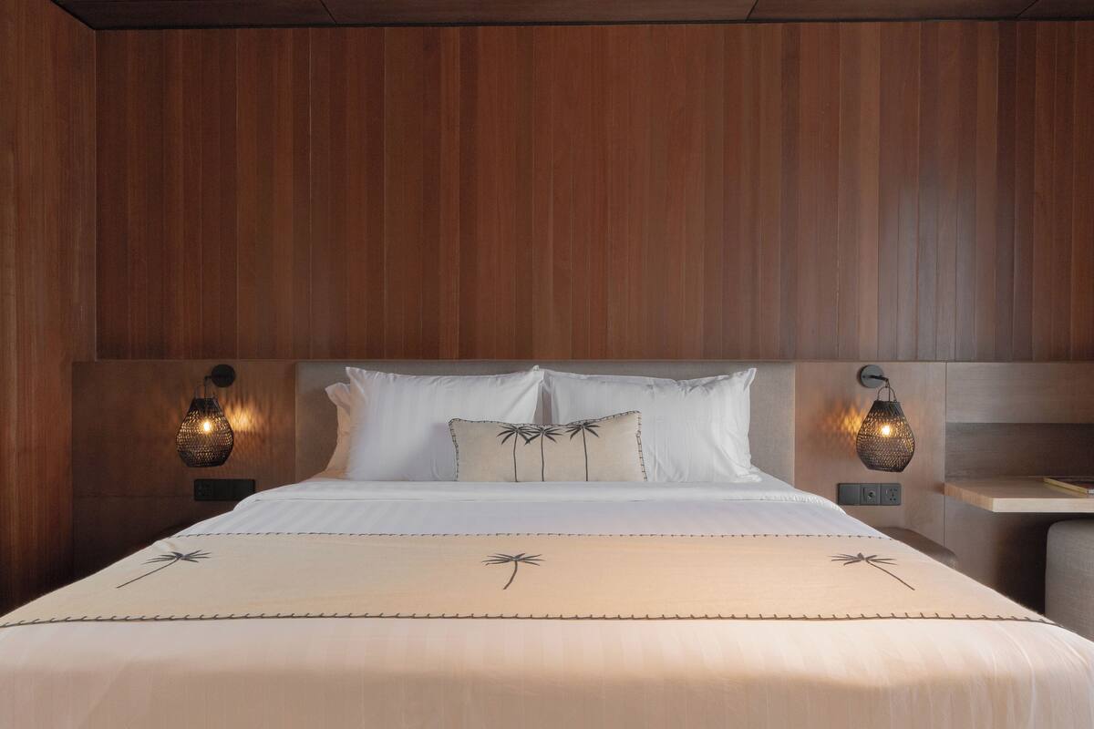 A hotel room with a wooden headboard, two bedside lamps, a bed with white linens, and a nightstand.