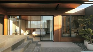 A modern hotel room with a large bed, a sitting area, and a view through the glass doors. - The Akasha Berawa Luxury Villas (Tibubeneng)