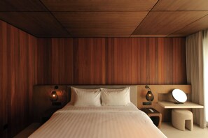 A bedroom with a wooden paneled headboard, a bed with white linens, bedside lamps, a nightstand, and a bedside table with a lamp. - The Akasha Berawa Luxury Villas (Tibubeneng)