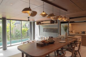 A modern kitchen with a wooden island, pendant lighting, and a view of a pool. - The Akasha Berawa Luxury Villas (Tibubeneng)